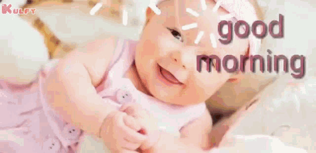 a baby in a pink dress is smiling and laying on a bed with the words `` good morning '' written on it .