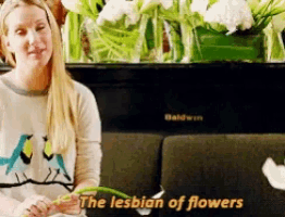 a woman is sitting on a couch holding a flower and the words " the lesbian of flowers " are above her