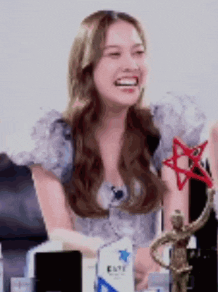 a woman is sitting at a table with a statue and a trophy and smiling .