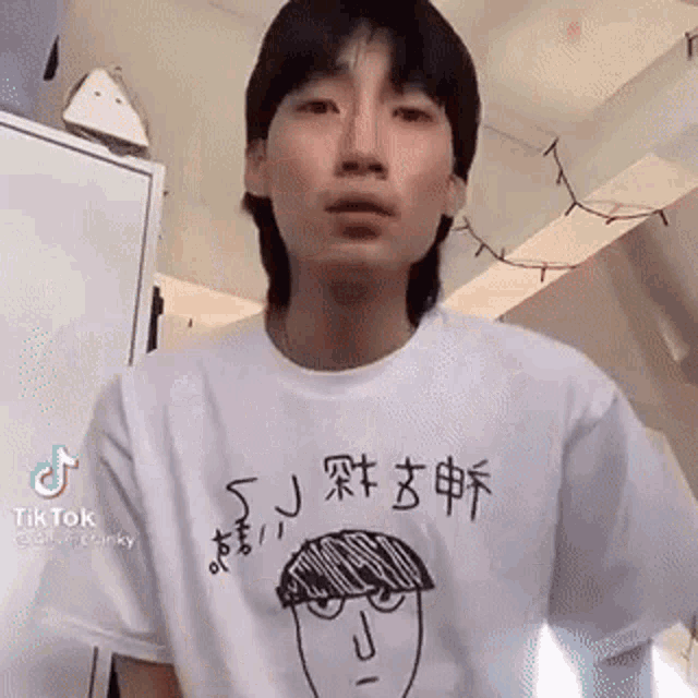 a young man wearing a white t-shirt with a drawing of a face on it is standing in a room .