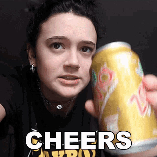a woman is holding a can of soda and the word cheers is on the bottom right
