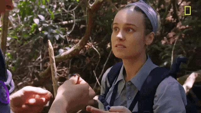 a woman with a backpack is standing in the woods looking at a snake in her hand .