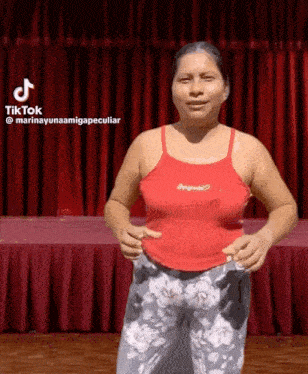 a woman in a red tank top and floral pants is standing on a stage .