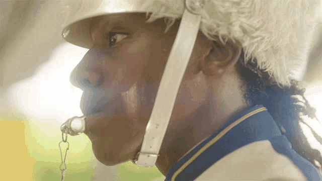 a close up of a man wearing a helmet with a whistle in his mouth