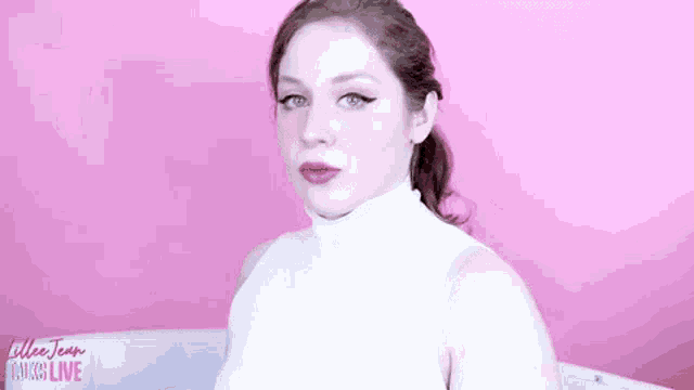 a woman wearing a white turtleneck sweater is sitting on a pink couch .