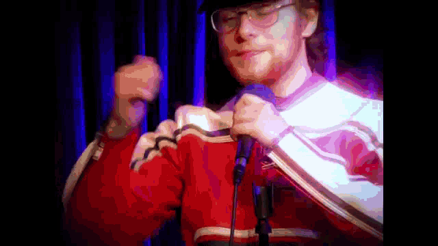 a man in a red and white sweater is holding a microphone in front of a blue curtain