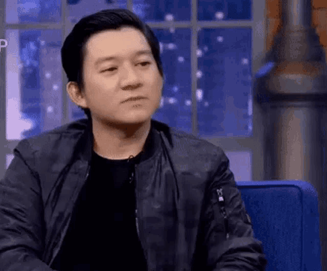a man in a black jacket is sitting in a chair .