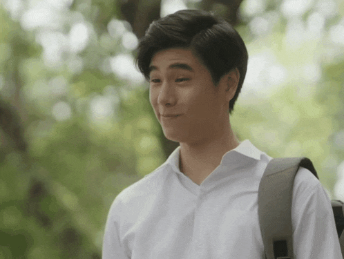 a man wearing a white shirt and carrying a backpack makes a funny face