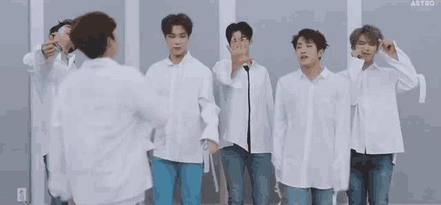 a group of young men are standing next to each other wearing white shirts and jeans .