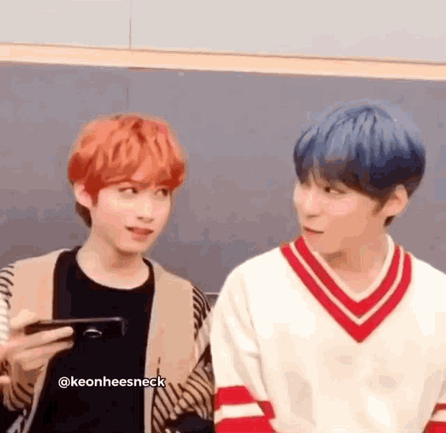 two young men are standing next to each other and one of them is holding a cell phone in his hand .
