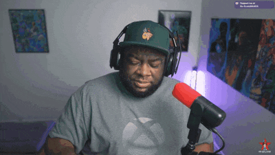 a man wearing headphones and a green hat with a pineapple on it sits in front of a microphone