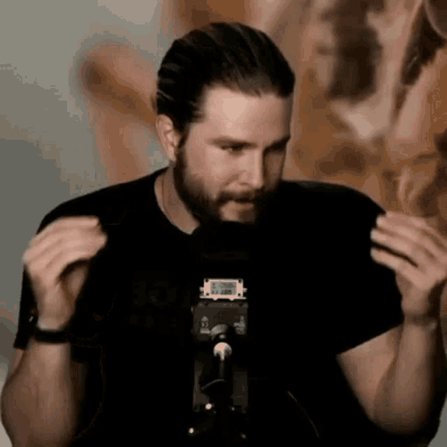 a man with a beard is standing in front of a microphone and talking into it