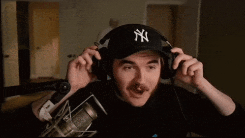 a man wearing a ny hat and headphones looks at the camera