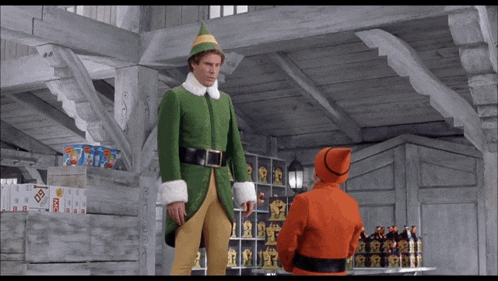 a man in a green elf costume is standing next to a man in an orange santa suit