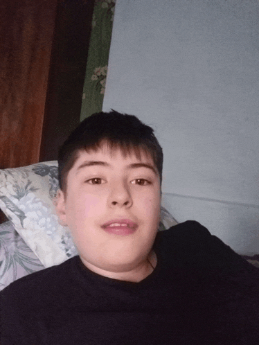 a boy in a black shirt is laying on a bed with a floral pillow