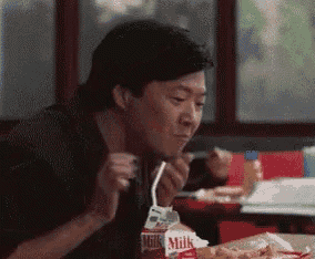 a man is sitting at a table drinking milk through a straw .