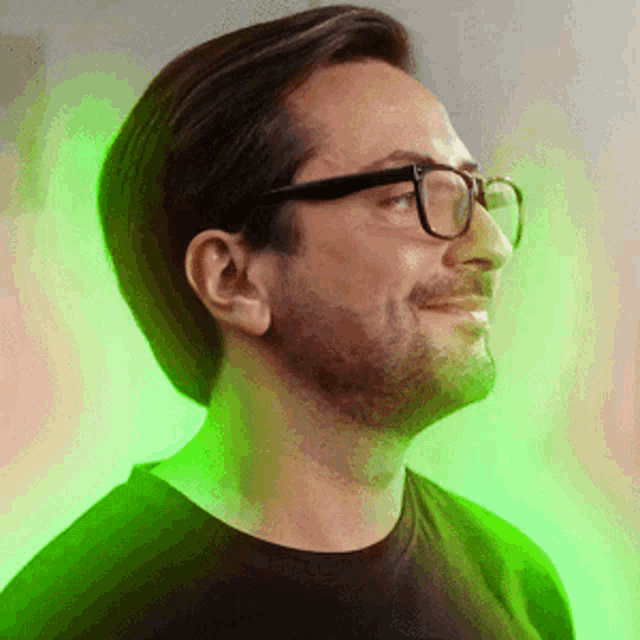 a man wearing glasses and a black shirt is smiling in front of a green light .