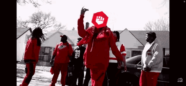 a man wearing a red jacket with a fist on it stands in front of a group of people