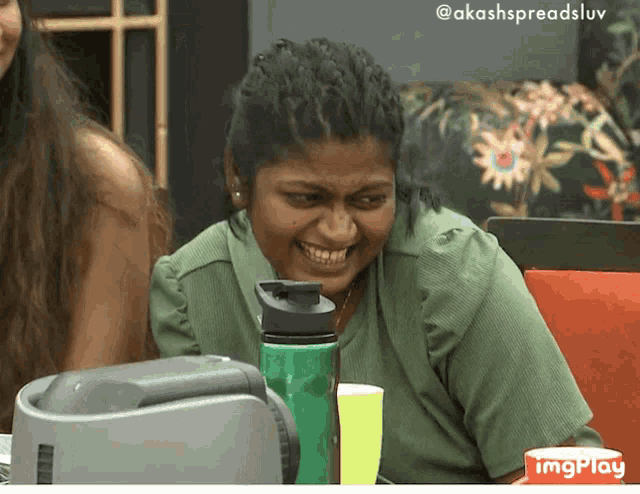 a woman in a green shirt is smiling while sitting at a table with a bottle of water