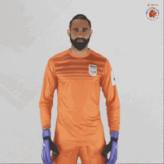 a man with a beard is wearing an orange shirt and gloves with a logo on the front