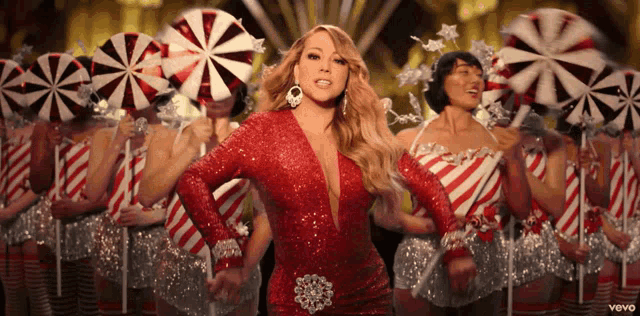 a woman in a red dress stands in front of a group of women in candy cane costumes