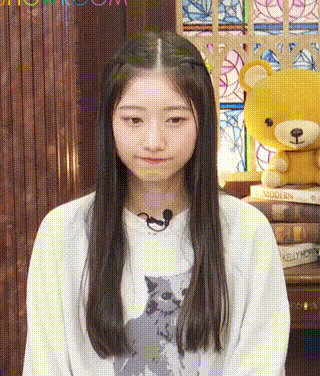 a girl wearing a white sweater with a cat on it is standing in front of a teddy bear .