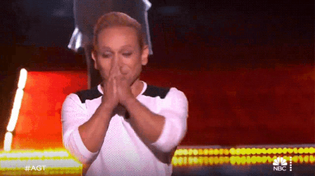 a woman covering her mouth with her hands on a stage with a nbc logo behind her