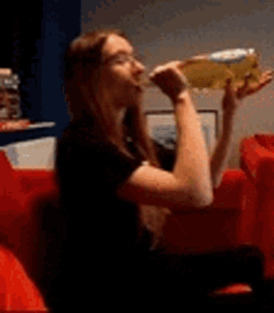 a woman is drinking from a bottle of beer while sitting on a red couch .