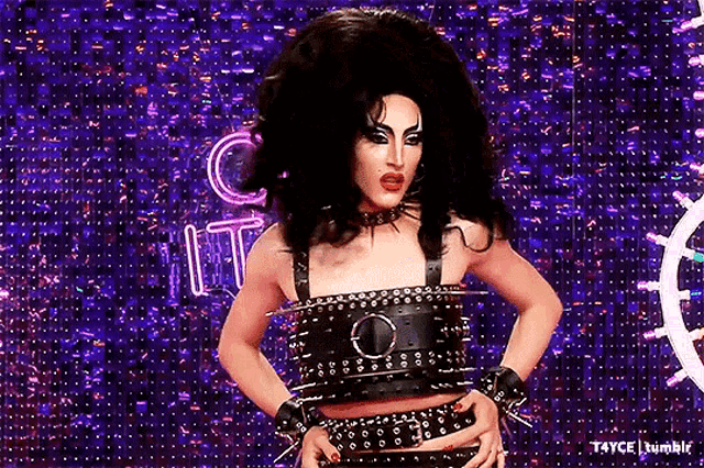 a drag queen is wearing a crop top with spikes on it and a choker .