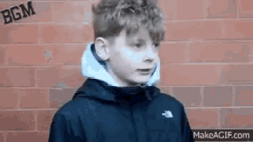 a young boy is standing in front of a brick wall .
