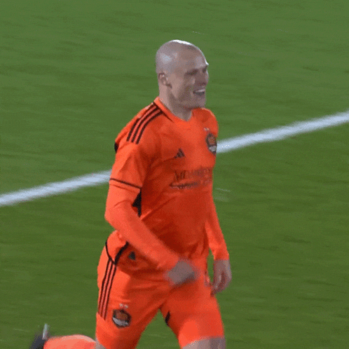 a soccer player wearing an orange adidas jersey is smiling on the field
