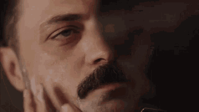a man with a mustache is shaving his face with a razor and soap .