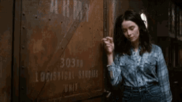 a woman in a plaid shirt is leaning against a wooden wall .