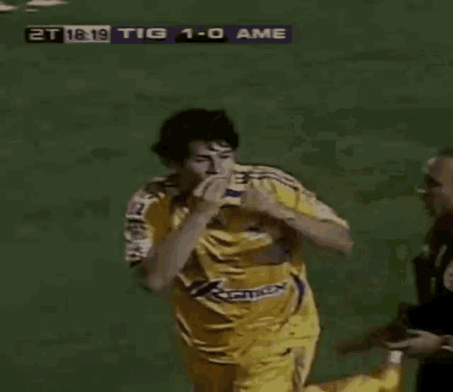 a soccer player in a yellow jersey is running on a field during a game between tigres and ame