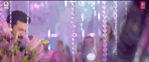 a man is standing in front of a crowd in a room with purple lights hanging from the ceiling .