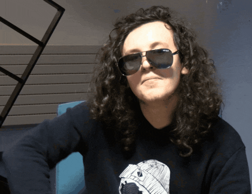 a man with long curly hair wearing sunglasses and a black sweatshirt