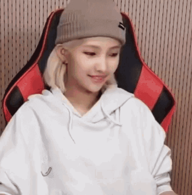 a girl wearing a beanie and a white hoodie is sitting in a chair .