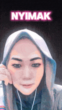 a woman wearing a hijab and ear buds stands in front of a neon sign that says nyimak