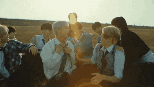 a group of young men are sitting in a field with the sun behind them