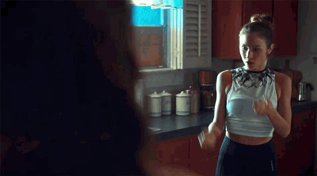 a woman in a white tank top is standing in a kitchen with red cabinets