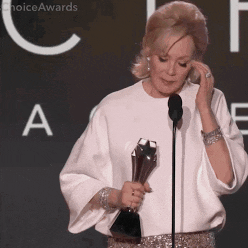 a woman is holding a trophy in front of a microphone with choiceawards written on the bottom