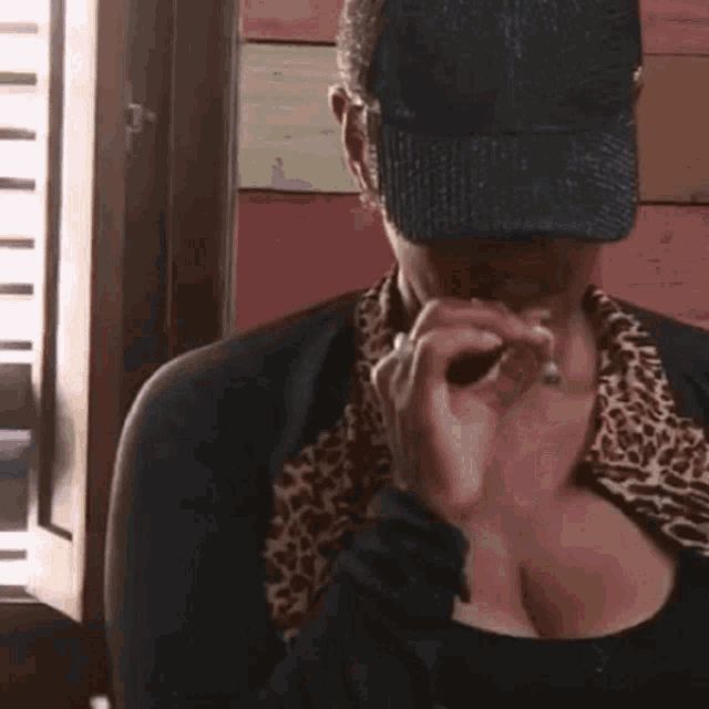 a woman wearing a hat and a leopard print shirt is holding a glass .