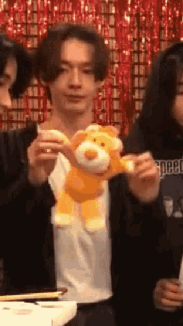 a man is holding a stuffed animal in his hands in front of a curtain .