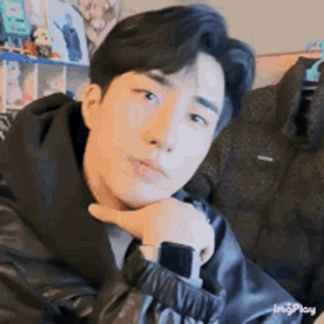 a young man wearing a black jacket and a smart watch is sitting on a couch .