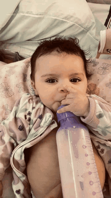 a baby is drinking from a purple bottle with measurements on it