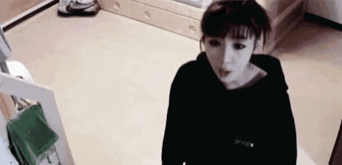 a woman in a black hoodie is standing in a room with a green towel on the floor .