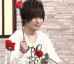 a young man is holding two red roses in his hands .