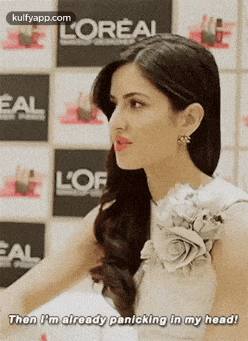 a woman in a white dress is standing in front of a wall with a flower on her shoulder .