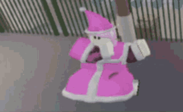 a pink and white cartoon character is standing in front of a fence wearing a santa hat .