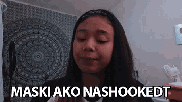 a girl says maski ako nashookedt in front of a wall tapestry